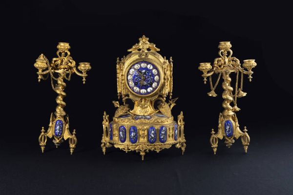 TRITTICO : H cm 32 e 30 composto da pendola da tavolo e coppia di candelieri a tre luci in bronzo dorato con inserti ovali e tondi in porcellana  con decori ad armi e scudi; quadrante in porcellana con numeri romani Difetti  Da revisionare  Quadrante firmato H. Te Ancelj a Tolouse  - Asta Asta 204 Orologi - Associazione Nazionale - Case d'Asta italiane