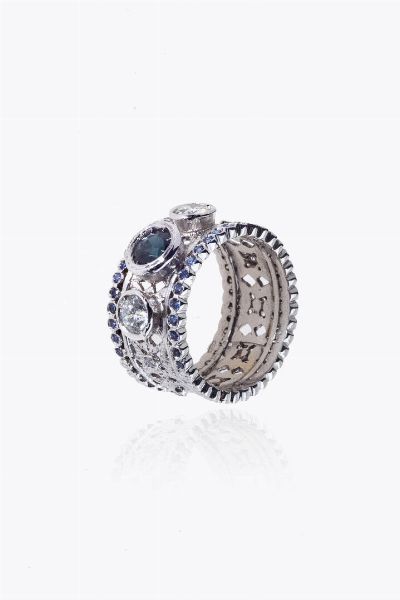 ANELLO : Peso gr 9 0 Misura 14 (54) in oro bianco  a fascia  con al centro uno zaffiro rotondo di ct 0 60 ca  ai lati due diamanti taglio brillante per totali ct 0 75 ca e quattro zirconi a decoro  - Asta Asta 205 Gioielli - Associazione Nazionale - Case d'Asta italiane