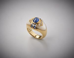 . - Anello in oro giallo 750/1000  e base di madreperla bianca con zaffiro centrale blu cabochon di circa 1,00 carati e zaffiri  blu laterali taglio carr e diamanti bianchi taglio a brillante ct.0,14.