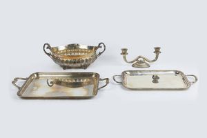 LOTTO DI QUATTRO OGGETTI IN ARGENTO - Peso complessivo gr 3169 8 Composto da: - 1 centrotavola di forma ovale con manici a volute; corpo bombato e lavorato.  [..]