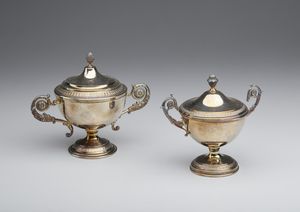 ARGENTIERE ITALIANO DEL XX SECOLO - Coppia di piccole zuccheriere in argento di diverse dimensioni, corpo ad urna decorato a motivi neoclassici, prese laterali in forma di spirali fitomorfe