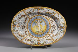 MANIFATTURA DI DERUTA - Piatto ovale in maiolica policroma decorato con putto alato armato di arco entro medaglione circolare contornato da decori a raffaellesche
