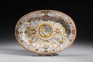 MANIFATTURA DI DERUTA - Piatto ovale in maiolica policroma decorato con putto alato a riposo entro medaglione circolare contornato da decori a grottesche e a volute