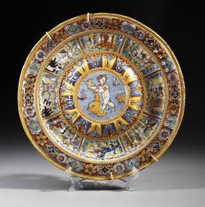 MANIFATTURA DI DERUTA - Grande piatto da pompa, centro umbonato con bacellature nel cavetto, decorato al centro da figura di putto su delfino entro medaglione e nel cavetto da riquadri raffiguranti putti alati contro animali