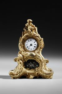 MANIFATTURA FRANCESE DEL XIX SECOLO - Piccolo orologio da tavolo in bronzo dorato in stile Luigi XV, ornato da volute e decorazioni floreali, sormontato da una figura di putto