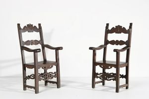 MANIFATTURA TOSCANA DEL XVII SECOLO - Coppia di scranni in legno di noce intagliato con schienale a cartelle sagomate, montanti a motivo fogliato, braccioli a giorno, gambe raccordate da cartella traforata