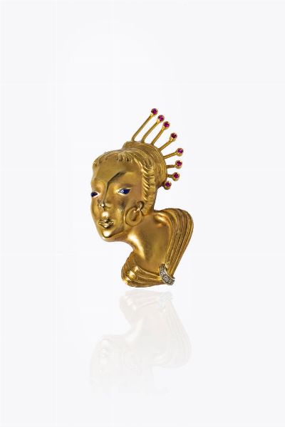 SPILLA : Peso gr 11 2 Cm 5x3 in oro giallo satinato  raffigurante un volto orientale. recante acconciatura con gemme rosse taglio rotondo e due diamanti taglio 8/8  - Asta Gioielli - Associazione Nazionale - Case d'Asta italiane