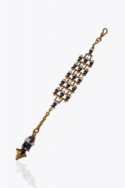 PORTACHIAVI : Peso gr 17 4 in oro 9 Kt; corpo composto da cinque file di mori in smalto policromo  terminante con ciondolo raffigurante il busto di un moro in smalto policromo. Granato taglio ovale a decoro  - Asta Gioielli - Associazione Nazionale - Case d'Asta italiane