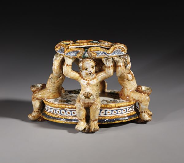 BOTTEGA DEI PATANAZZI, URBINO, FINE DEL XVI SECOLO : Saliera in maiolica policroma poggiante su base ovale su cui si trovano quattro putti seduti che sorreggono l'invaso superiore, decorato nell'incavo da una figura allegorica in grisaille  - Asta Asta 387 | ARTE ANTICA E DEL XIX SECOLO - DAL RINASCIMENTO AL SIMBOLISMO: OPERE DA COLLEZIONI ITALIANE Tradizionale - Associazione Nazionale - Case d'Asta italiane