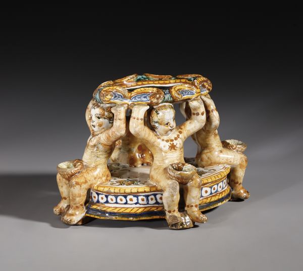 BOTTEGA DEI PATANAZZI, URBINO, FINE DEL XVI SECOLO : Saliera in maiolica policroma poggiante su base ovale su cui si trovano quattro putti seduti che sorreggono l'invaso superiore, decorato nell'incavo da una figura allegorica in grisaille  - Asta Asta 387 | ARTE ANTICA E DEL XIX SECOLO - DAL RINASCIMENTO AL SIMBOLISMO: OPERE DA COLLEZIONI ITALIANE Tradizionale - Associazione Nazionale - Case d'Asta italiane