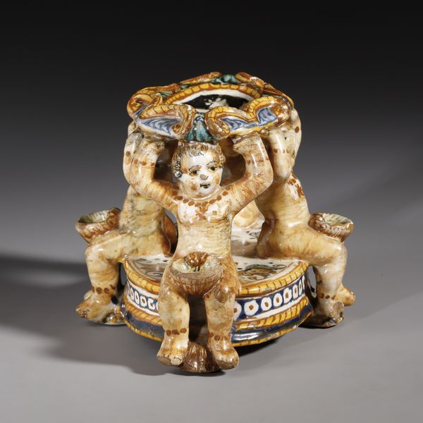 BOTTEGA DEI PATANAZZI, URBINO, FINE DEL XVI SECOLO : Saliera in maiolica policroma poggiante su base ovale su cui si trovano quattro putti seduti che sorreggono l'invaso superiore, decorato nell'incavo da una figura allegorica in grisaille  - Asta Asta 387 | ARTE ANTICA E DEL XIX SECOLO - DAL RINASCIMENTO AL SIMBOLISMO: OPERE DA COLLEZIONI ITALIANE Tradizionale - Associazione Nazionale - Case d'Asta italiane