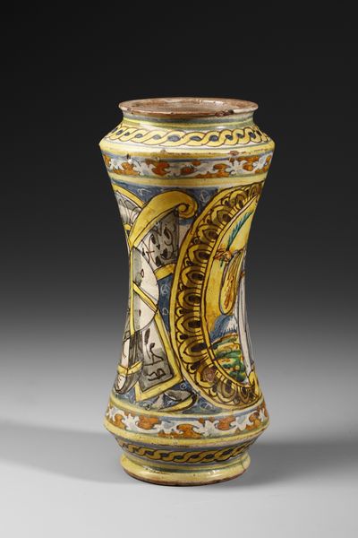 MANIFATTURA DI COLLESANO DEL XVII SECOLO : Albarello in maiolica policroma di forma a rocchetto, sul fronte figura di santa martire entro medaglione ovale su fondo giallo, contornato da decori a trofei su fondo blu  - Asta Asta 387 | ARTE ANTICA E DEL XIX SECOLO - DAL RINASCIMENTO AL SIMBOLISMO: OPERE DA COLLEZIONI ITALIANE Tradizionale - Associazione Nazionale - Case d'Asta italiane