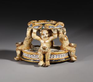 BOTTEGA DEI PATANAZZI, URBINO, FINE DEL XVI SECOLO - Saliera in maiolica policroma poggiante su base ovale su cui si trovano quattro putti seduti che sorreggono l'invaso superiore, decorato nell'incavo da una figura allegorica in grisaille