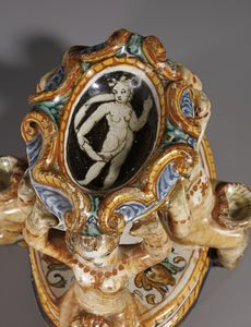 BOTTEGA DEI PATANAZZI, URBINO, FINE DEL XVI SECOLO : Saliera in maiolica policroma poggiante su base ovale su cui si trovano quattro putti seduti che sorreggono l'invaso superiore, decorato nell'incavo da una figura allegorica in grisaille  - Asta Asta 387 | ARTE ANTICA E DEL XIX SECOLO - DAL RINASCIMENTO AL SIMBOLISMO: OPERE DA COLLEZIONI ITALIANE Tradizionale - Associazione Nazionale - Case d'Asta italiane