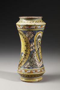 MANIFATTURA DI COLLESANO DEL XVII SECOLO : Albarello in maiolica policroma di forma a rocchetto, sul fronte figura di santa martire entro medaglione ovale su fondo giallo, contornato da decori a trofei su fondo blu  - Asta Asta 387 | ARTE ANTICA E DEL XIX SECOLO - DAL RINASCIMENTO AL SIMBOLISMO: OPERE DA COLLEZIONI ITALIANE Tradizionale - Associazione Nazionale - Case d'Asta italiane