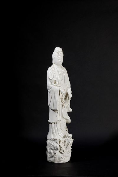Figura in porcellana Blanc de Chine raffigurante Guanyin eretta su con vasetto, ramo fiorito e drago sulla base, Cina, inizi XX secolo  - Asta Arte Orientale - Associazione Nazionale - Case d'Asta italiane