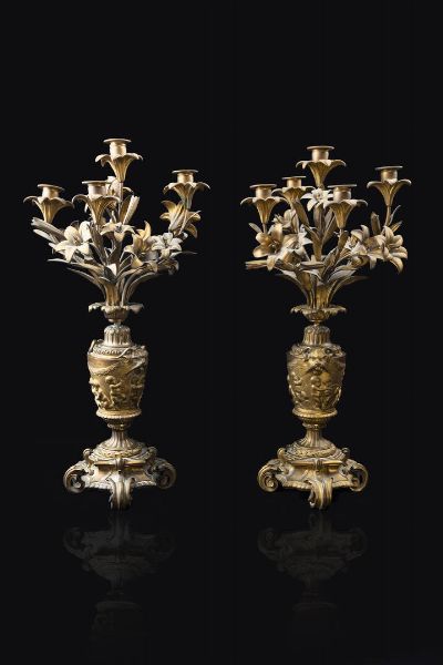 COPPIA DI CANDELIERI : H cm 62 in bronzo dorato (difetti) a cinque luci caduano  montate su gigli e foglie; parte centrale lavorata a vaso con manici antropomorfi e putti intenti nell'arte del gioco e della danza; base circolare decorata da foglie di alloro e poggiante su base a volute.  - Asta  Dipinti, argenti e antiquariato - Associazione Nazionale - Case d'Asta italiane