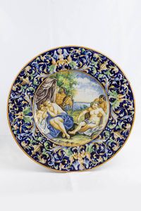 PIATTO DA PARATA - Diam. 55 cm in ceramica invetriata e dipinta con scena amorosa tra ninfe e fauni. Manifattura Deruta  siglato  [..]