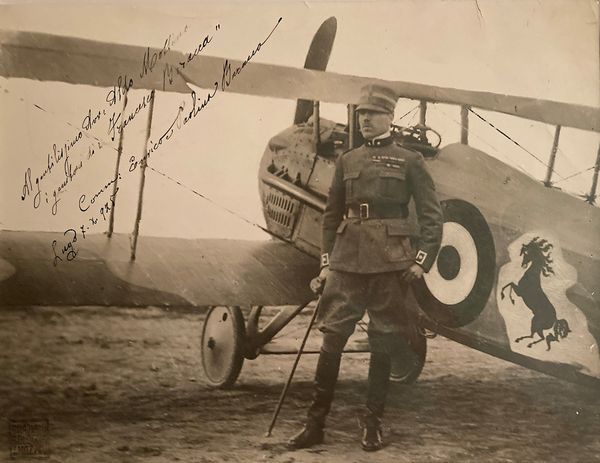 1925, fotografia cm. 24X32, incorniciata, che ritrae Francesco Baracca accanto al suo aereo SPAD S. XIII  - Asta Filatelia e Storia Postale - Associazione Nazionale - Case d'Asta italiane