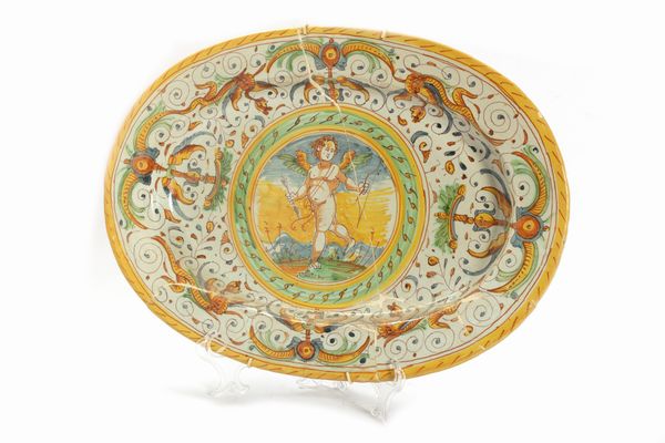 Piatto ovale in maiolica policroma decorato a grottesche e Cupido al centro  - Asta Incanti d'arte - Associazione Nazionale - Case d'Asta italiane