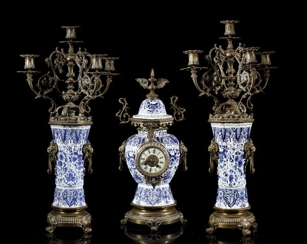 MANIFATTURA DEL XIX SECOLO : Trittico da camino in porcellana di Delft bianca e blu con inserti e montature in bronzo dorato, composto da orologio e due candelabri a quattro luci  - Asta Asta 395 | ARTE ANTICA E DEL XIX SECOLO Online - Associazione Nazionale - Case d'Asta italiane