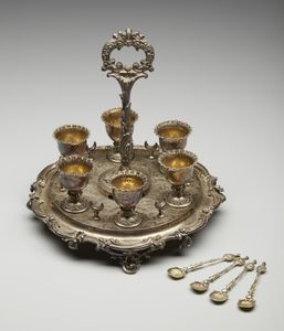 ARGENTIERE INGLESE DEL XIX SECOLO - Portauova in argento cesellato composto da 6 coppette e 4 cucchiaini, su vassoio circolare a decorazioni fitomorfe