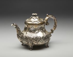 ARGENTIERE INGLESE DEL XIX SECOLO - Teiera in argento sbalzato, corpo piriforme con motivi floreali e fitomorfi a rilievo in stile settecentesco, poggiante su piedi a ricciolo