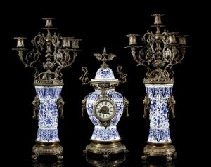 MANIFATTURA DEL XIX SECOLO - Trittico da camino in porcellana di Delft bianca e blu con inserti e montature in bronzo dorato, composto da orologio e due candelabri a quattro luci