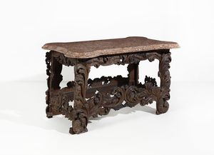 MANIFATTURA ITALIANA DEL XVII-XVIII SECOLO - Tavolo in legno intagliato in forma di volute e motivi fitomorfi, piano in marmo broccatello di Spagna