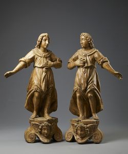 SCULTORE ITALIANO DEL XVII SECOLO - Coppia di angeli in legno scolpito poggianti su basi con volti di cherubini a rilievo tra volute