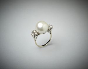 . - Anello in oro bianco 18 carati con perla bianca coltivata sferica e sei diamanti laterali taglio a brillante di circa 1 ct. totale.