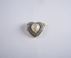 . - Spilla/ciondolo in oro giallo 18k con diamante taglio a cuore dal peso di 2 ct. ca. e contorno di pav di zaffiri intensi tondi blu dal peso di 3 ct. ca.