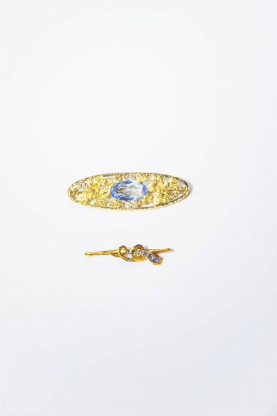LOTTO DI DUE SPILLE : -in oro 9 Kt  di forma ovale  con decori a racemi. al centro gemma blu sintetica. Peso gr 9 4. Cm 2x6 5 -in oro giallo a serpente con piccoli zaffiri. Peso gr 3 7. Lunghezza cm 4.  - Asta Gioielli - Associazione Nazionale - Case d'Asta italiane