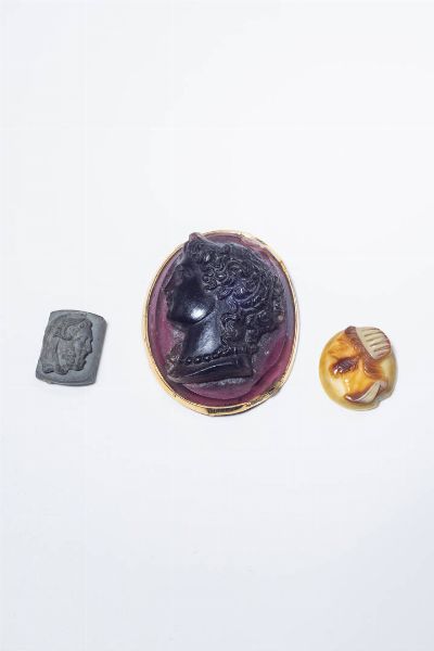 LOTTO DI TRE GIOIELLI : composto da: -cammeo in vetro viola raffigurante un ritratto femminile. Montatura in oro giallo. Cm 5x4. -cammeo su lastra di materiale grigio raffigurante volto virile di profilo. Cm 2x1. -cammeo in conchiglia con volto virile inciso. Cm 2 5x2.  - Asta Gioielli - Associazione Nazionale - Case d'Asta italiane