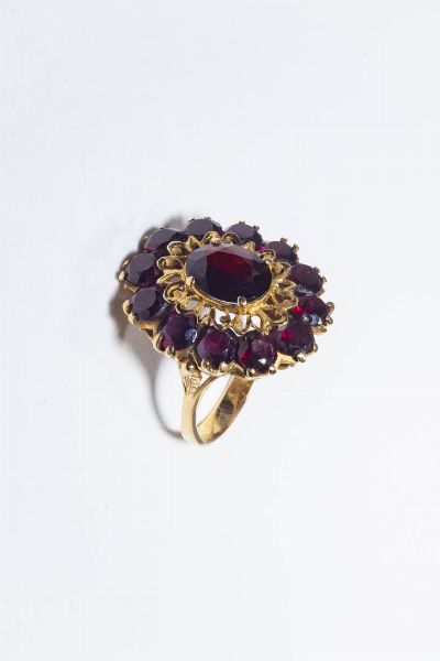 ANELLO : Peso gr10 4 Misura 17 (57) in oro giallo  anni '60  sommit ovale con granato centrale e granati taglio rotondo a decoro.  - Asta Gioielli - Associazione Nazionale - Case d'Asta italiane