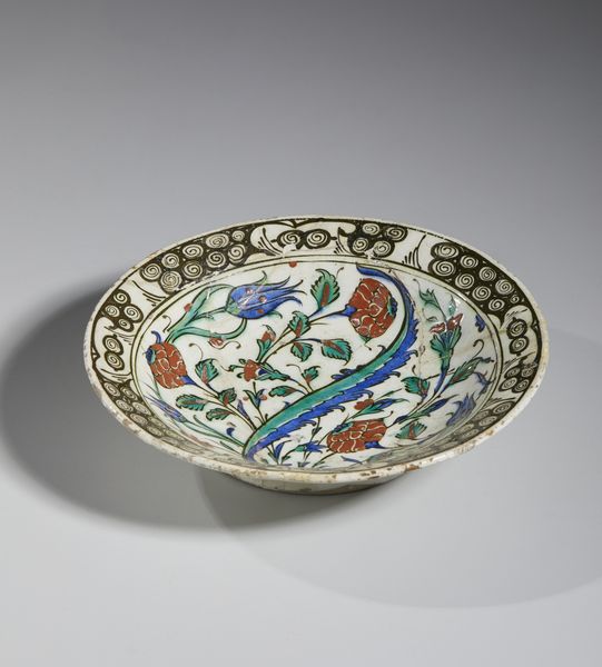 MANIFATTURA DI IZNIK, XVII SECOLO : Piatto in ceramica invetriata policroma con cavetto centrato da una foglia lanceolata attorniata da garofani rossi, tulipani blu e tralci fogliati, tesa decorata con motivo 'ad onde e scogli'  - Asta Asta 432 | ARTE ANTICA E DEL XIX SECOLO Tradizionale - Associazione Nazionale - Case d'Asta italiane