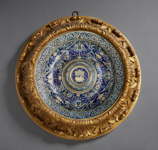 BOTTEGA DI MASTRO GIORGIO, GUBBIO, 1530 CIRCA : Piatto in maiolica dipinta e lustrata, cavetto decorato da motivi a trofei 'all'antica' e fitomorfi su fondo blu, con umbone centrato da stemma, tesa con fascia ondulata alternata a fiori stilizzati  - Asta Asta 432 | ARTE ANTICA E DEL XIX SECOLO Tradizionale - Associazione Nazionale - Case d'Asta italiane