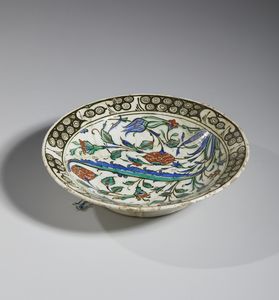 MANIFATTURA DI IZNIK, XVII SECOLO : Piatto in ceramica invetriata policroma con cavetto centrato da una foglia lanceolata attorniata da garofani rossi, tulipani blu e tralci fogliati, tesa decorata con motivo 'ad onde e scogli'  - Asta Asta 432 | ARTE ANTICA E DEL XIX SECOLO Tradizionale - Associazione Nazionale - Case d'Asta italiane
