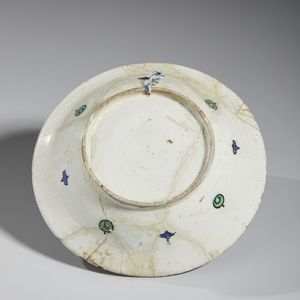 MANIFATTURA DI IZNIK, XVII SECOLO : Piatto in ceramica invetriata policroma con cavetto centrato da una foglia lanceolata attorniata da garofani rossi, tulipani blu e tralci fogliati, tesa decorata con motivo 'ad onde e scogli'  - Asta Asta 432 | ARTE ANTICA E DEL XIX SECOLO Tradizionale - Associazione Nazionale - Case d'Asta italiane