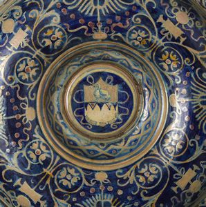 BOTTEGA DI MASTRO GIORGIO, GUBBIO, 1530 CIRCA : Piatto in maiolica dipinta e lustrata, cavetto decorato da motivi a trofei 'all'antica' e fitomorfi su fondo blu, con umbone centrato da stemma, tesa con fascia ondulata alternata a fiori stilizzati  - Asta Asta 432 | ARTE ANTICA E DEL XIX SECOLO Tradizionale - Associazione Nazionale - Case d'Asta italiane