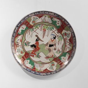 ARTE GIAPPONESE - Grande piatto in porcellana decorato in policromia al centro con personaggi sotto un elegante pergolato di glicine contornato da un ricco bordo di riserve sovrapposte a vari decori. Giappone, XIX sec. periodo Meiji.