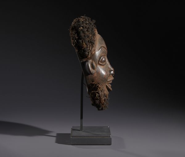 Bamoun - Camerun (Grassland) : Nello stile di Maschera-copricapo antropomorfa in legno duro a patina scura, fibre e capelli  - Asta Asta 444 | AFRICA, OCEANIA E AMERICHE - ARTIGIANATO AFRICANO: VARI COMMITTENTI E SELEZIONE DALLA COLLEZIONE BARTOLOMUCCI Online - Associazione Nazionale - Case d'Asta italiane