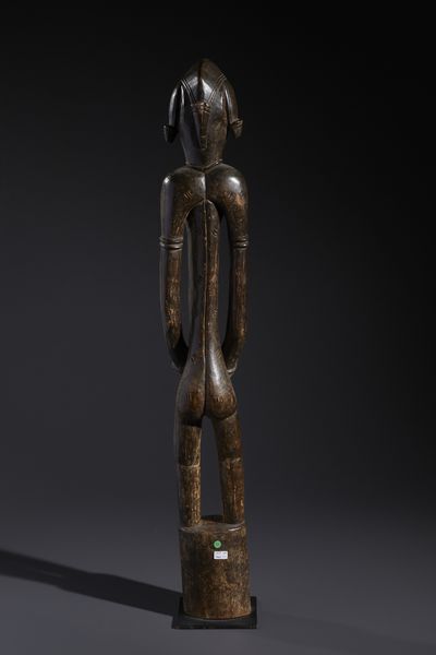 Senufo - Costa d'Avorio/Mali/Burkina Faso : Nello stile di Grande scultura antropomorfa su basamento  in legno duro a patina marrone  - Asta Asta 444 | AFRICA, OCEANIA E AMERICHE - ARTIGIANATO AFRICANO: VARI COMMITTENTI E SELEZIONE DALLA COLLEZIONE BARTOLOMUCCI Online - Associazione Nazionale - Case d'Asta italiane