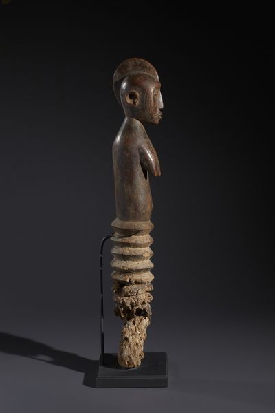 Mossi - Burkina Faso : Nello stile di Grande palo con figura antropomorfa femminile  in legno duro a patina bruno-rossastra  - Asta Asta 444 | AFRICA, OCEANIA E AMERICHE - ARTIGIANATO AFRICANO: VARI COMMITTENTI E SELEZIONE DALLA COLLEZIONE BARTOLOMUCCI Online - Associazione Nazionale - Case d'Asta italiane