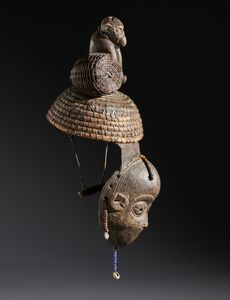 Igbo - Nigeria : Nello stile di Maschera con copricapo sormontato da una scultura di scimmia  in legno a patina scura, fibre,  conchiglie, perline, semi e pelle  - Asta Asta 444 | AFRICA, OCEANIA E AMERICHE - ARTIGIANATO AFRICANO: VARI COMMITTENTI E SELEZIONE DALLA COLLEZIONE BARTOLOMUCCI Online - Associazione Nazionale - Case d'Asta italiane