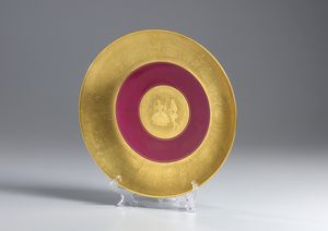 MANIFATTURA TEDESCA DEL XX SECOLO - Piatto decorativo in porcellana parzialmente dorata e dipinta, con scene a rilievo in stile settecentesco