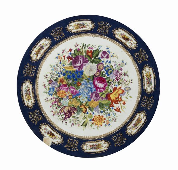 MANIFATTURA DEL XX SECOLO : Grande piano circolare in ceramica dipinto e decorato nello stile di Limoges con trionfo di fiori al centro, fascia esterna a fondo blu con riquadri raffiguranti nature morte di strumenti musicali  - Asta Asta 469 | ARTE ANTICA E DEL XIX SECOLO Online - Associazione Nazionale - Case d'Asta italiane