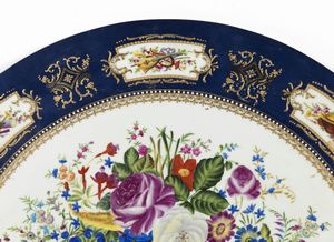 MANIFATTURA DEL XX SECOLO : Grande piano circolare in ceramica dipinto e decorato nello stile di Limoges con trionfo di fiori al centro, fascia esterna a fondo blu con riquadri raffiguranti nature morte di strumenti musicali  - Asta Asta 469 | ARTE ANTICA E DEL XIX SECOLO Online - Associazione Nazionale - Case d'Asta italiane