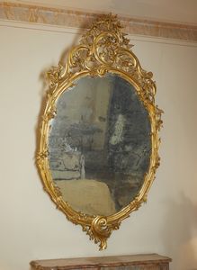 MANIFATTURA DEL XIX SECOLO - Grande specchiera in legno intagliato e dorato, cornice e cimasa decorate a motivi floreali e a volute
