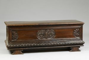 MANIFATTURA LOMBARDA DEL XVII SECOLO - Cassapanca in legno di noce intagliato, con riserva centrale raffigurante stemma nobiliare, due riserve laterali a forma di conchiglia.